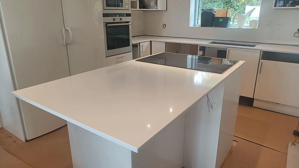 Köksbänkskiva i vit Technistone Crystal Absolute White, polerad kvartskomposit, med köksö och svart häll i Glumslöv.