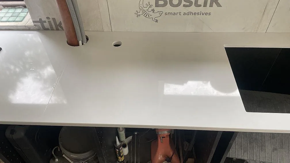 Blank yta i vit Technistone Crystal Absolute White komposit med hällöppning och rörgenomföring i köket i Härryda.