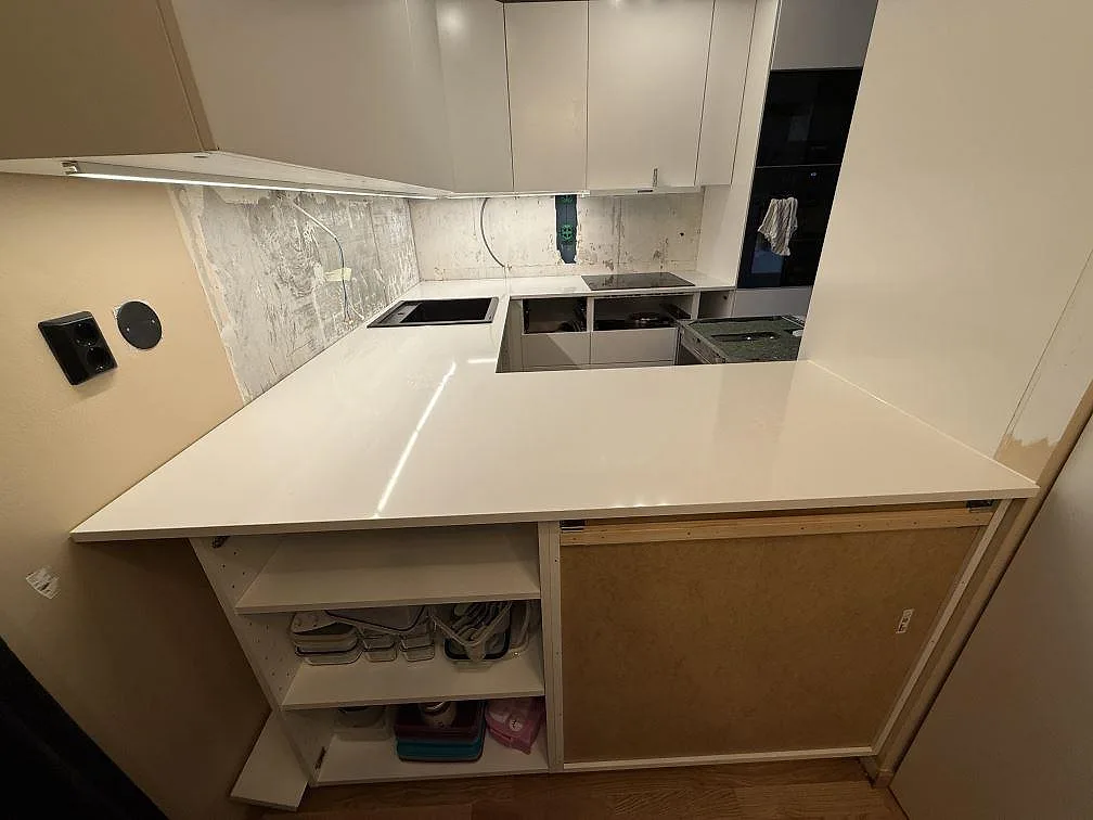 Köksbänkskiva i vit Technistone Crystal Absolute White, polerad kvartskomposit, med halvö, diskho och häll under montering i Kungsängen.