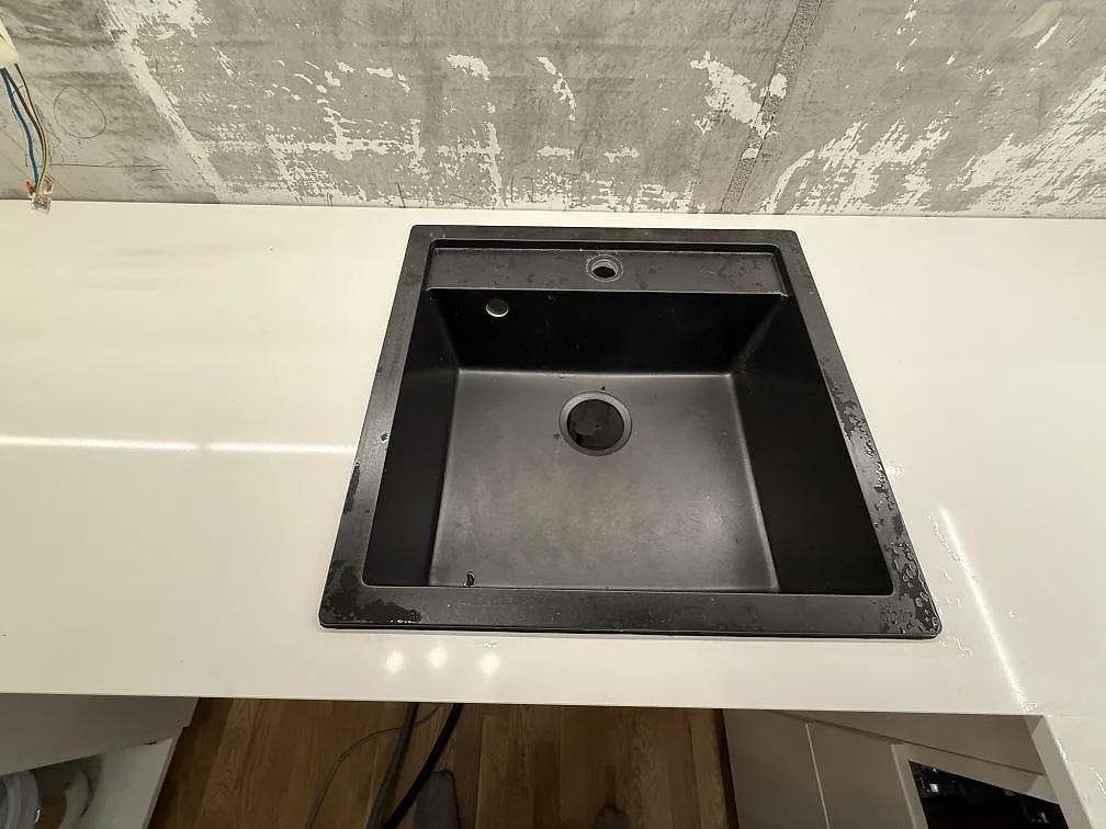 Närbild av mörk diskho i polerad vit Technistone Crystal Absolute White, monterad i köksbänkskiva under arbete i Kungsängen.