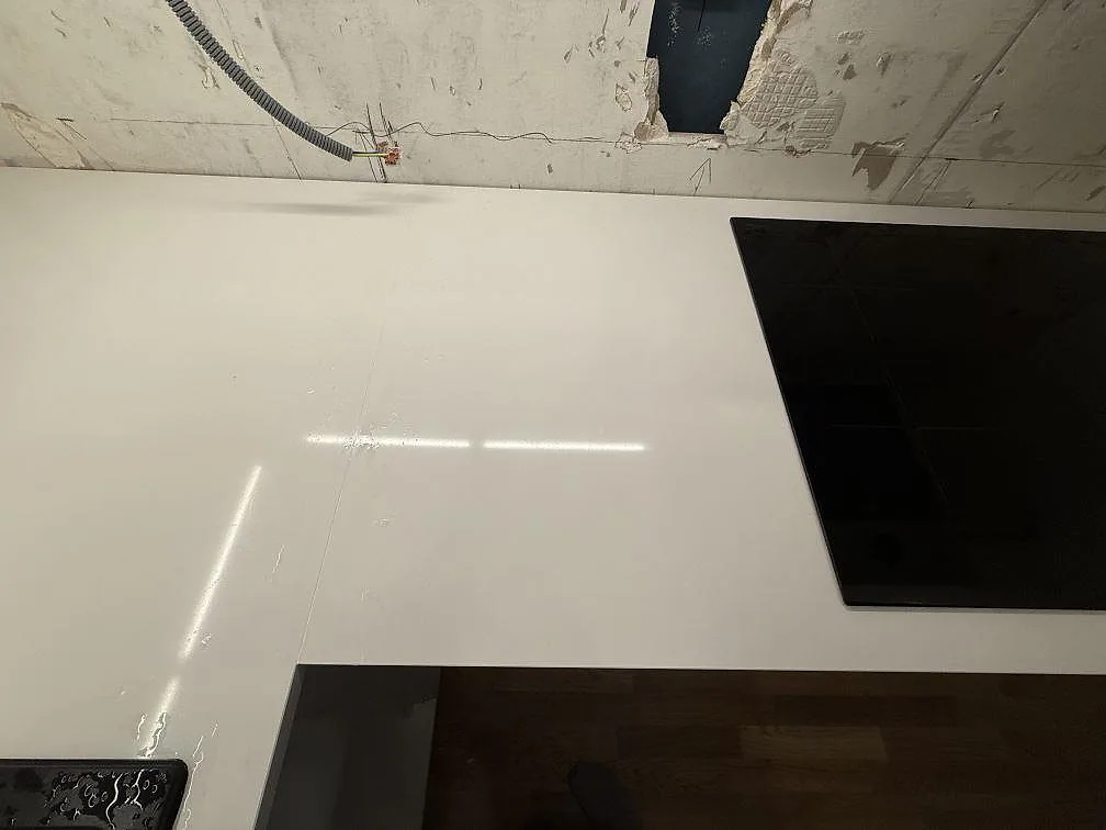 Detalj av vit polerad kvartskompositbänkskiva i Kungsängen med häll, diskho och synlig väggyta under pågående montering.