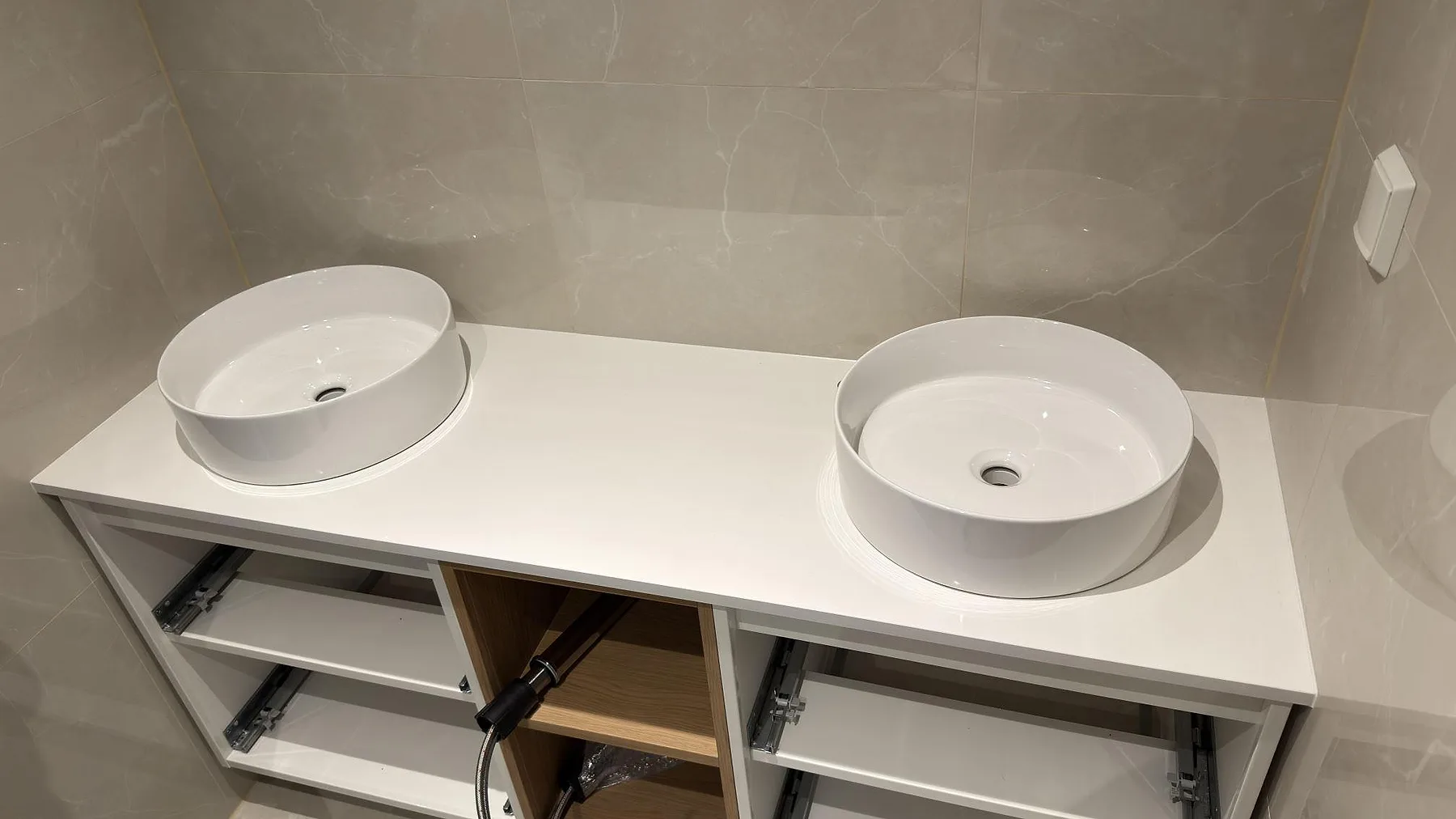 Bänkskiva i vit Technistone Crystal Absolute White komposit, polerad, med två runda ovanpåliggande tvättställ i ett badrum i Örebro.