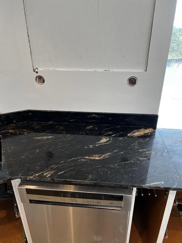 Detalj av polerad mörk Technistone-komposit ovanför inbyggnadsugn och öppna trästommar i kök i Uddevalla.