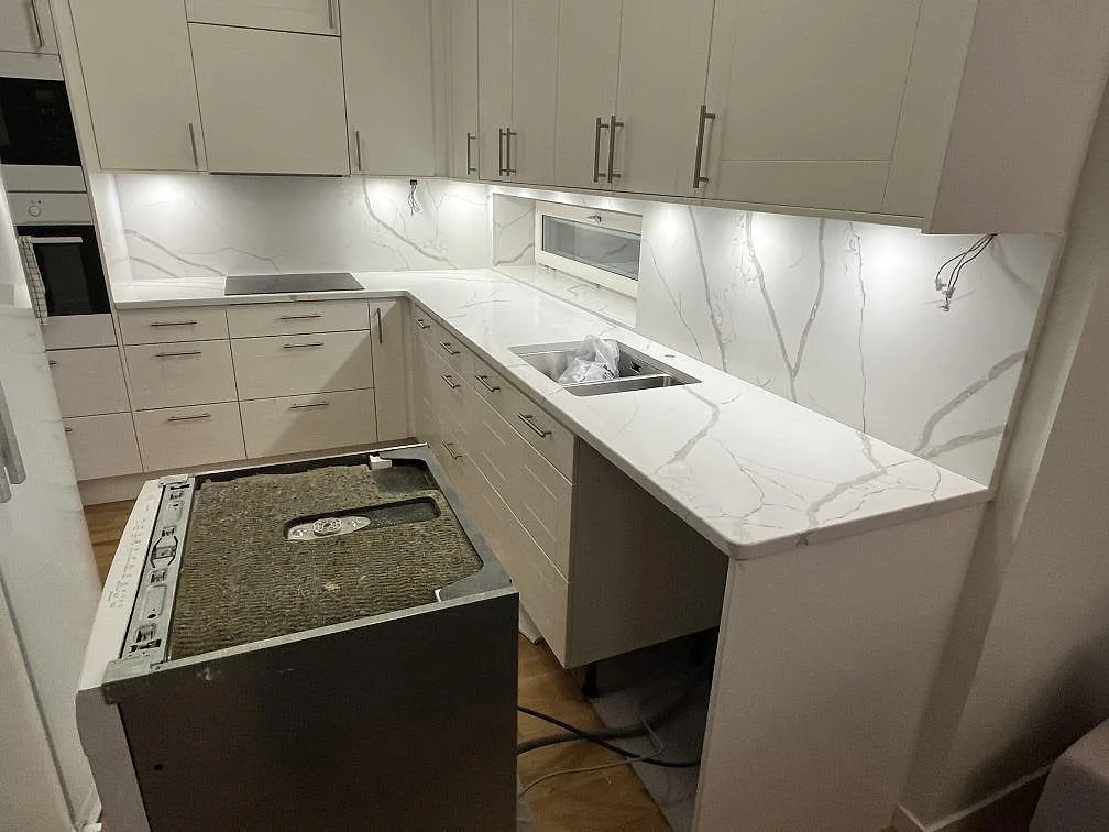 Köksbänkskiva i Technistone Crystal Calacatta Silva, polerad vit komposit med grå ådring, under montering i ett kök i Kungsholmen, Stockholm.