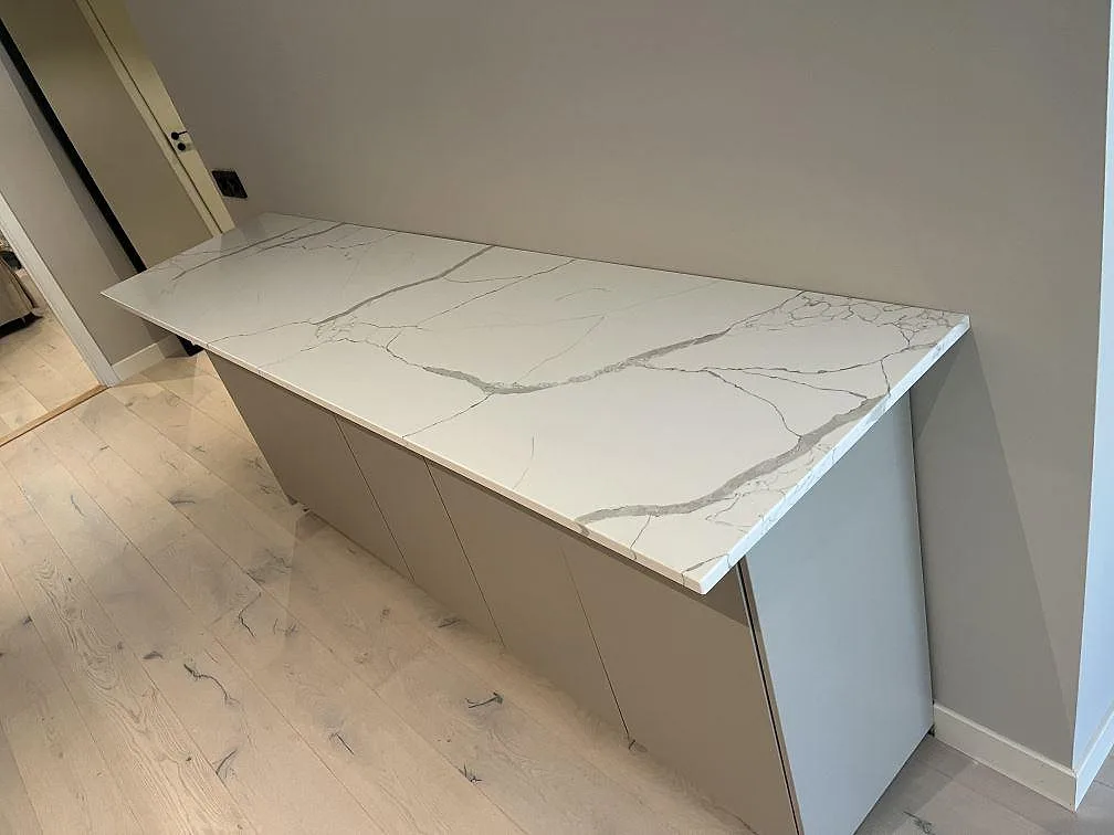 Köksbänkskiva i vit Technistone Crystal Calacatta Silva, polerad komposit, med neddragen gavel på en köksö i Stocksund.