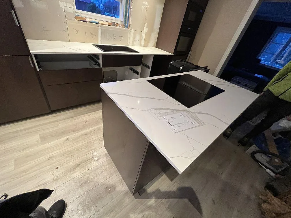 Köksbänkskiva i vit Technistone Crystal Calacatta Silva, polerad komposit, med köksö och induktionshäll i ett kök i Valskog.