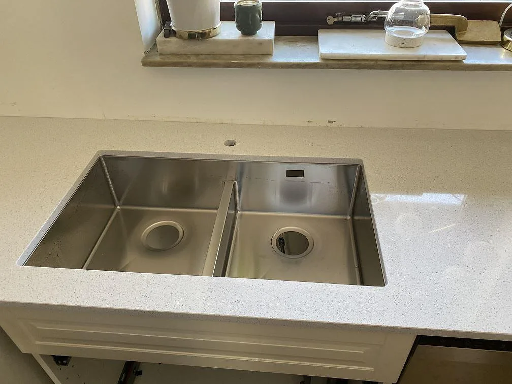 Underlimmad rostfri dubbelho i en vit polerad köksbänkskiva av Technistone Crystal Quartz White framför ett fönster i ett kök i Malmö.