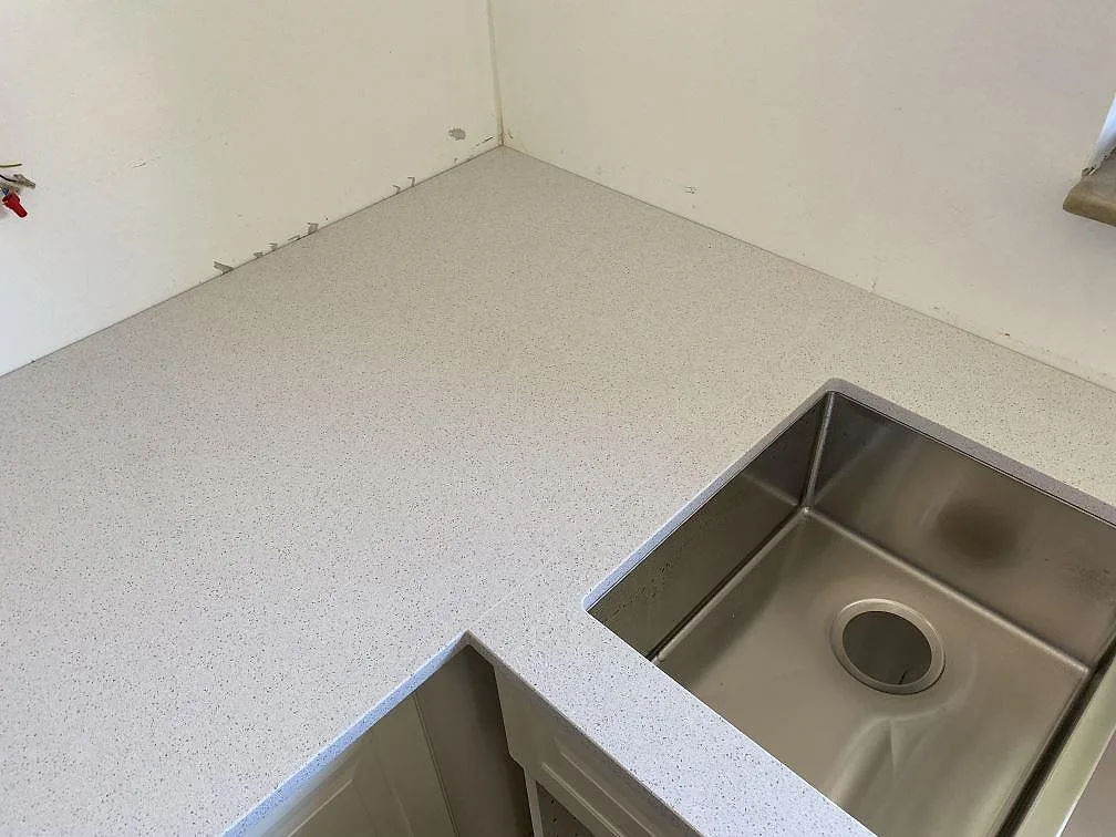 Hörnparti av en vit polerad köksbänkskiva i Technistone Crystal Quartz White med underlimmad rostfri diskho i ett kök i Malmö.