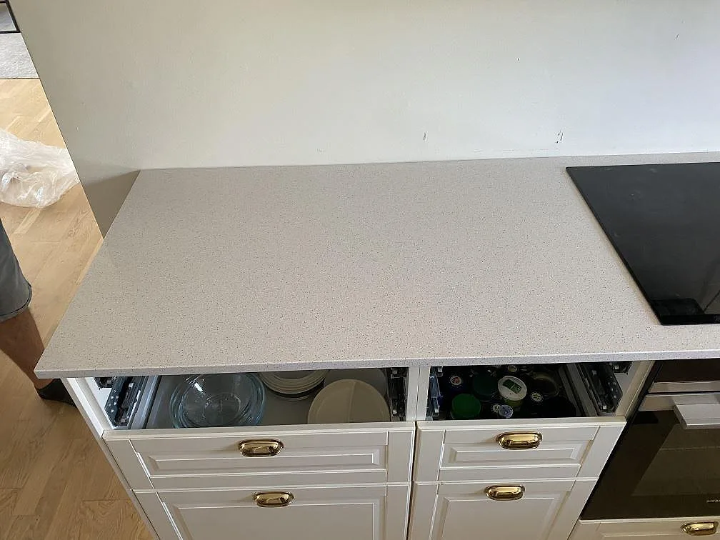 Polerad köksbänkskiva i vit Technistone Crystal Quartz White med infälld induktionshäll och öppna lådor under montering i ett kök i Malmö.