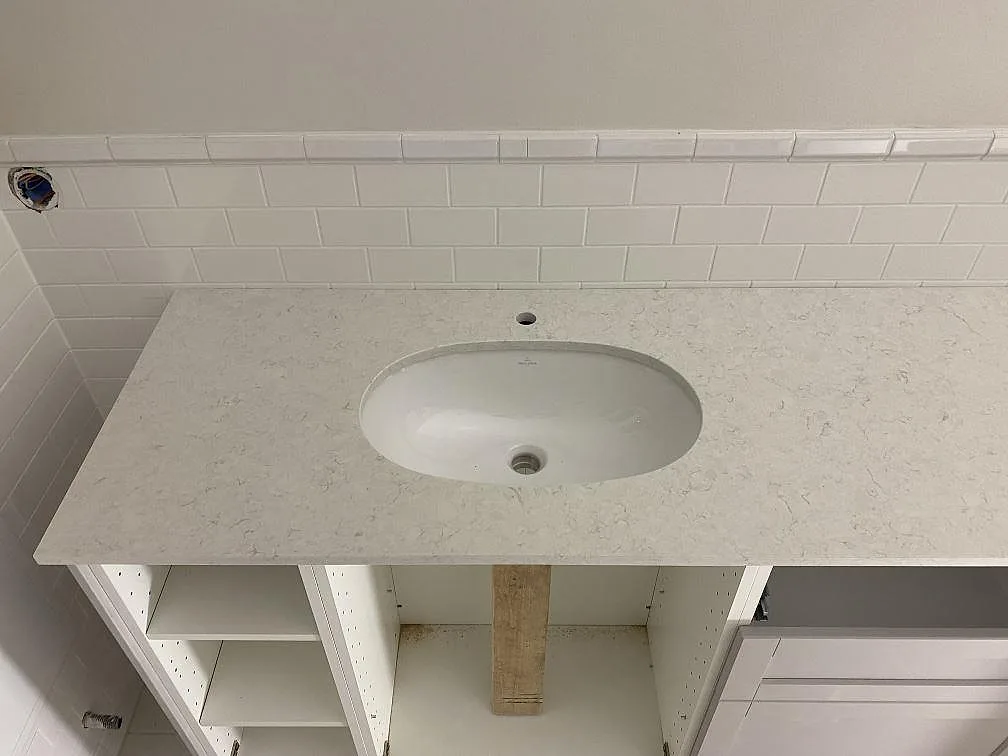 Närbild på polerad Technistone Glencoe runt ett vitt tvättställ, ljus komposit med grå ådring i Ängelholm.