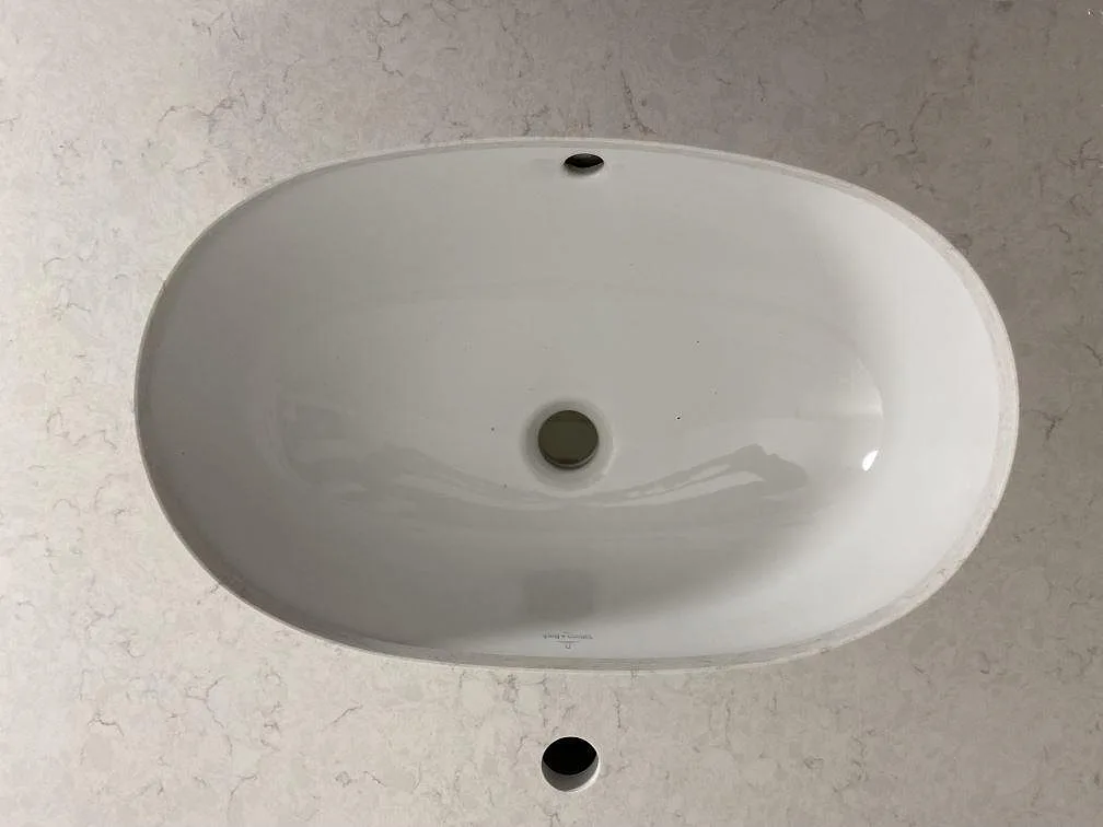Tät detalj på vitt tvättställ i polerad Technistone Glencoe med synlig grå teckning i kompositstenen.