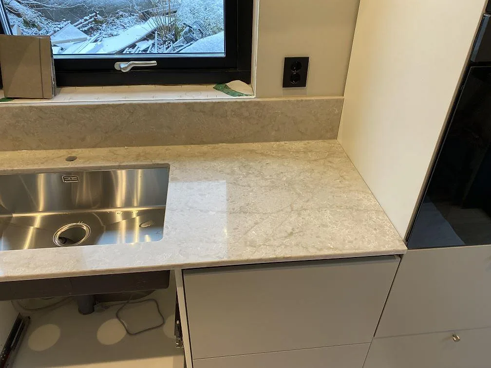 Sidovy av köksbänkskiva i polerad Technistone Glencoe med rostfri diskho och ljus stenstruktur i Alafors.