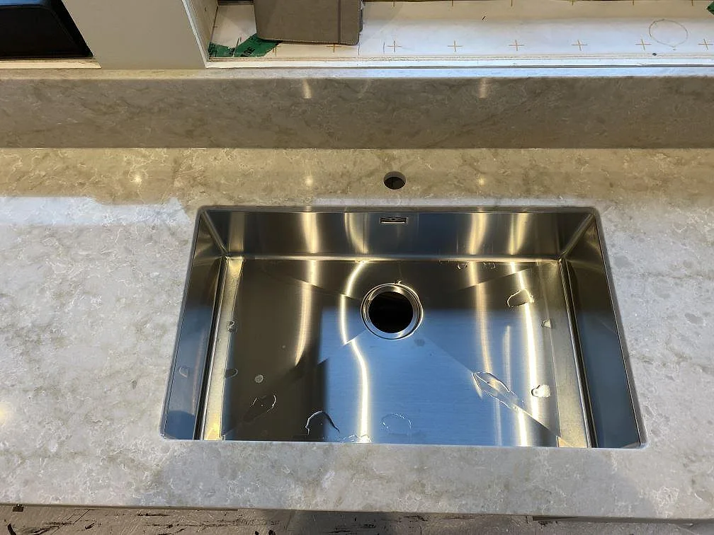 Detaljbild av rostfri diskho och hål för blandare i polerad Technistone Glencoe komposit i Alafors.