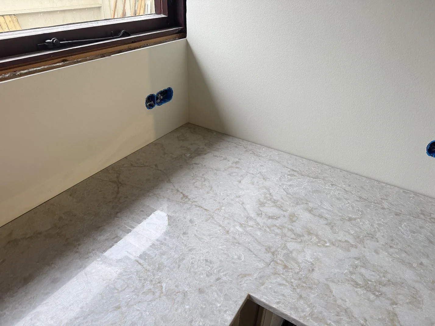 Hörn av köksbänkskiva i polerad Technistone Glencoe, ljus komposit med grå ådring, under ett fönster i Birkerød.