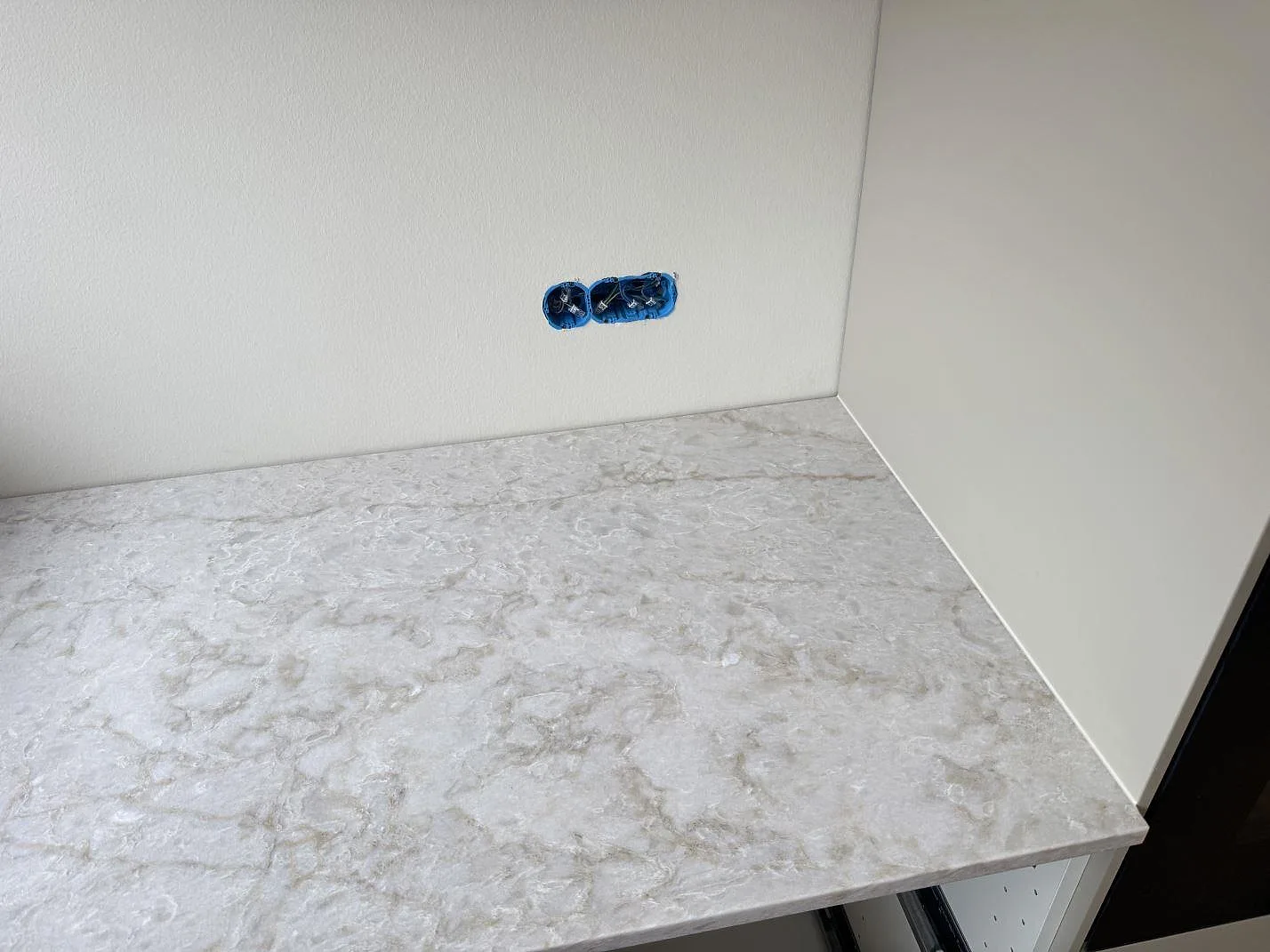 Närbild av polerad Technistone Glencoe köksbänkskiva med ljus grå ådring och vägguttag ovanför i Birkerød.