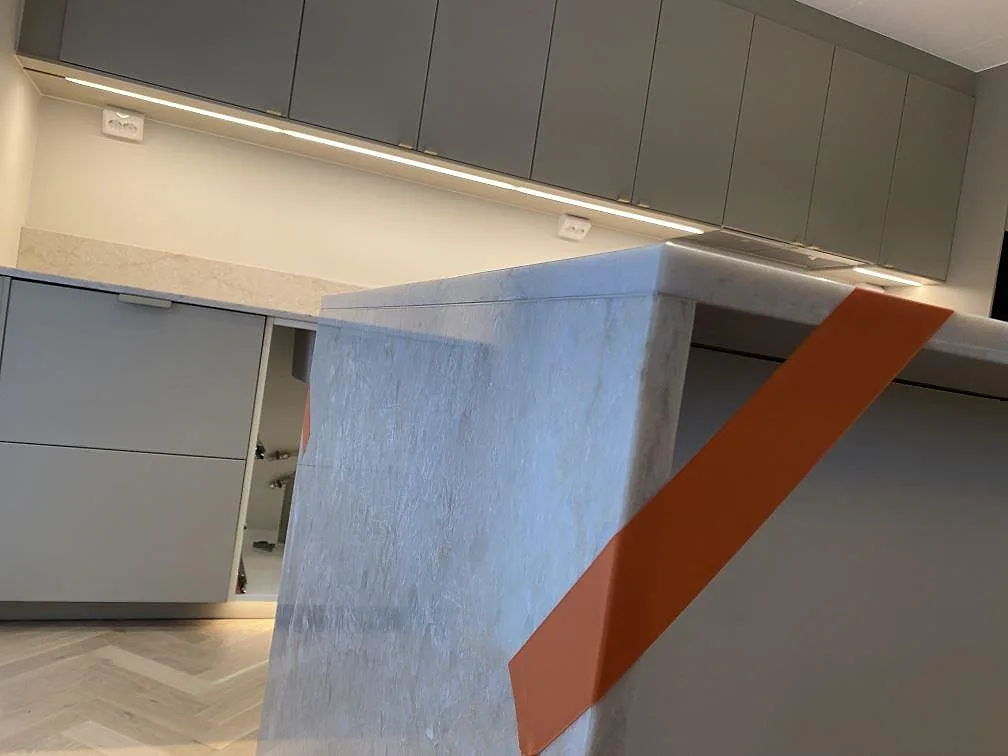 Detalj av klädd köksögavel i polerad Technistone Glencoe, kvartskomposit med ljus grå ådring, under montering i Bunkeflostrand.