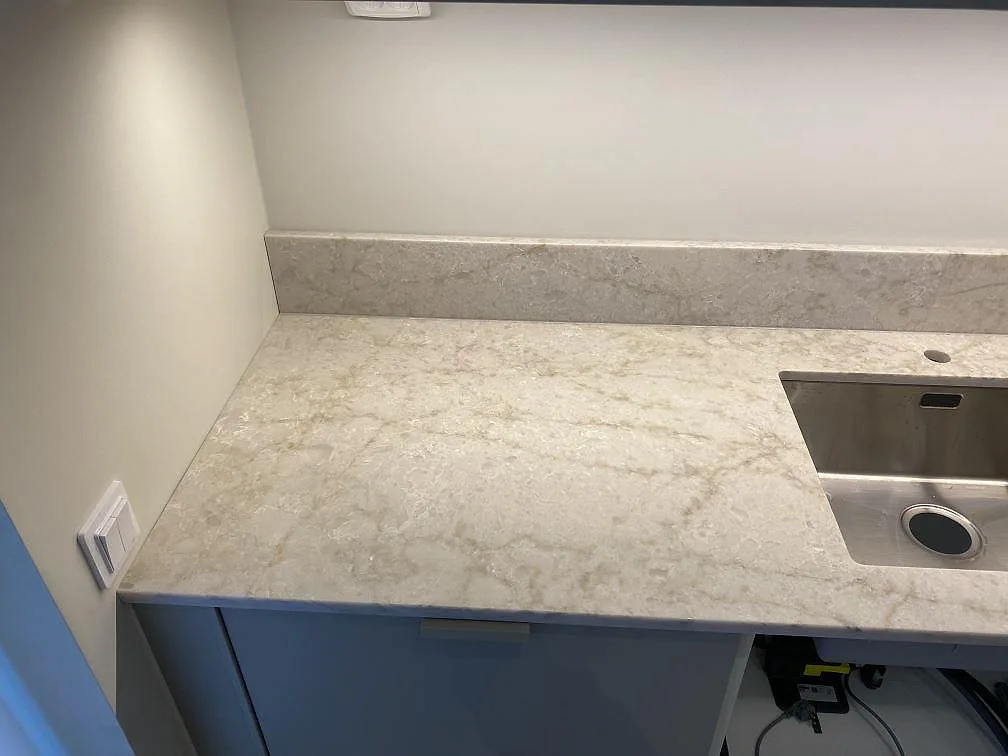 Närbild av polerad Technistone Glencoe bänkskiva, ljus kvartskomposit, vid rostfri diskho och stänkkant i Bunkeflostrand.