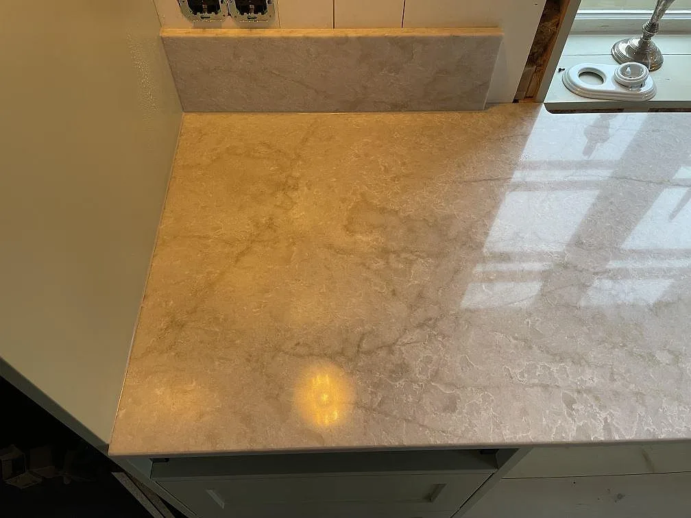 Närbild av polerad Technistone Glencoe som köksbänkskiva med uppvikt stänkkant och ljus ådring i Karlholmsbruk.