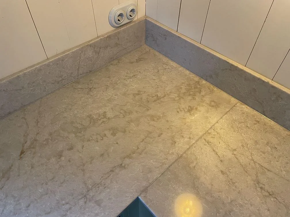 Hörn på köksbänkskiva i polerad Technistone Glencoe med kort stänkkant och mjuk grå ådring i Karlholmsbruk.