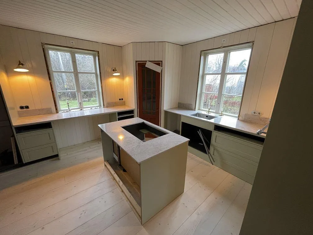 Köksbänkskiva och köksö i polerad Technistone Glencoe, ljus kvartskomposit med diskret ådring, i ett kök under montering i Karlholmsbruk.