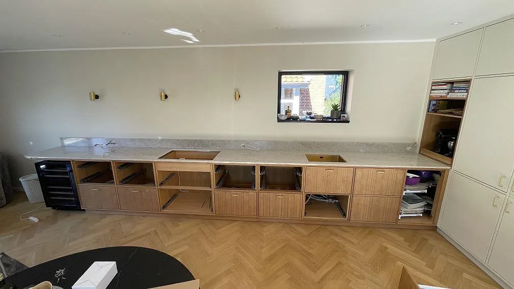 Lång köksbänkskiva i polerad Technistone Glencoe med uppvikt stänkkant och synliga urtag i ett kök i København S.