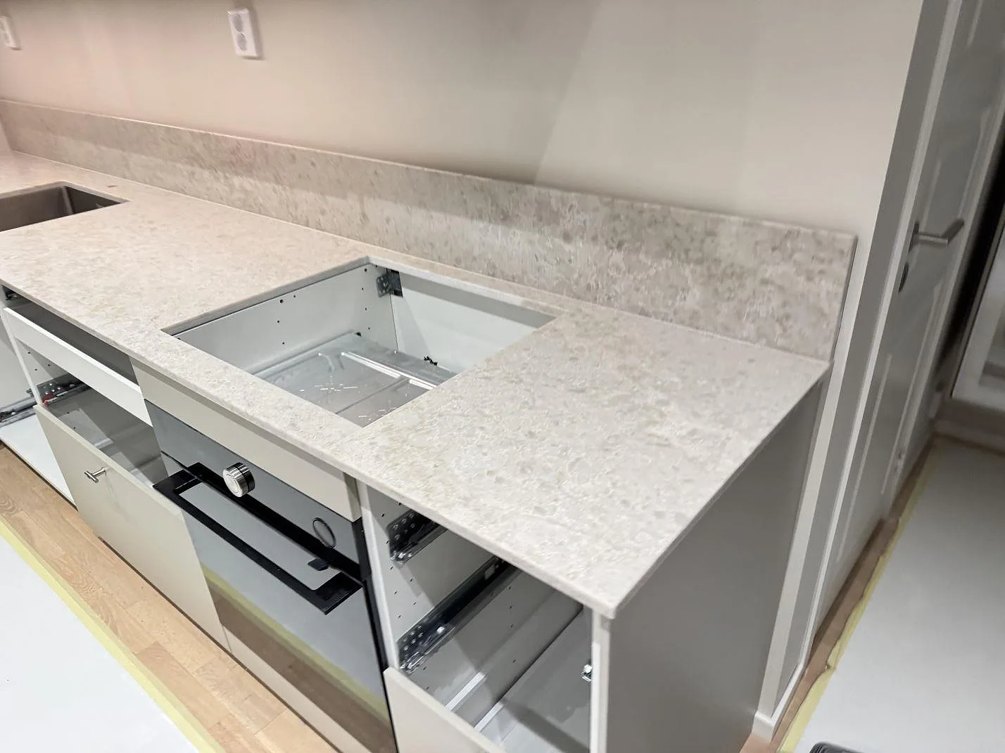 Köksbänkskiva i polerad Technistone Glencoe, ljus kvartskomposit, med uppvikt stänkkant och rostfri diskho i Lomma.