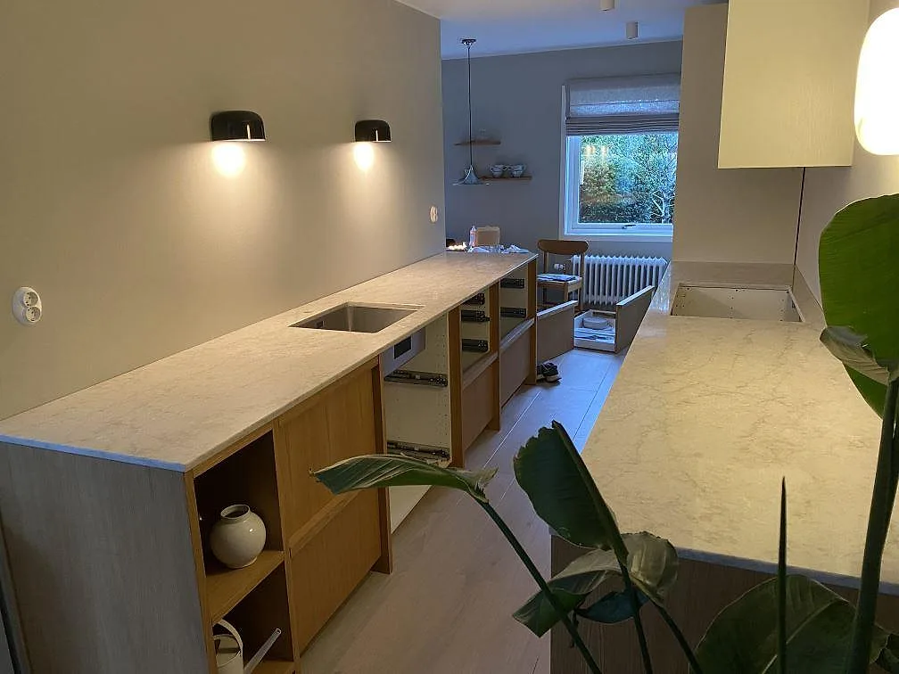 Översikt av kök i Malmö med ljus Technistone Glencoe som polerad kompositbänkskiva, rostfri diskho och öppet urtag i motstående bänk.