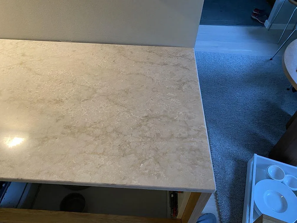 Hörndetalj av köksbänkskiva i polerad Technistone Glencoe, ljus kvartskomposit på öppna stommar under montering i Malmö.