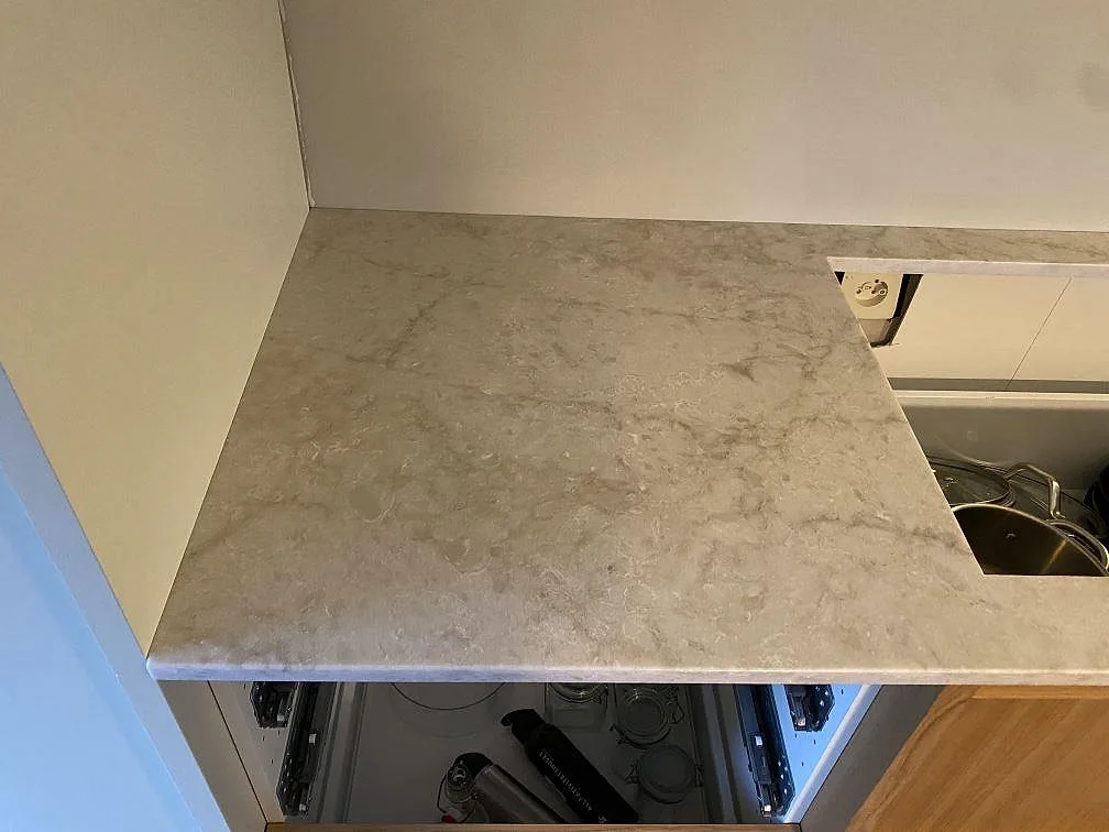 Arbetsyta i polerad Technistone Glencoe vid vägg och öppna köksstommar, ljus kvartskomposit under montering i Malmö.