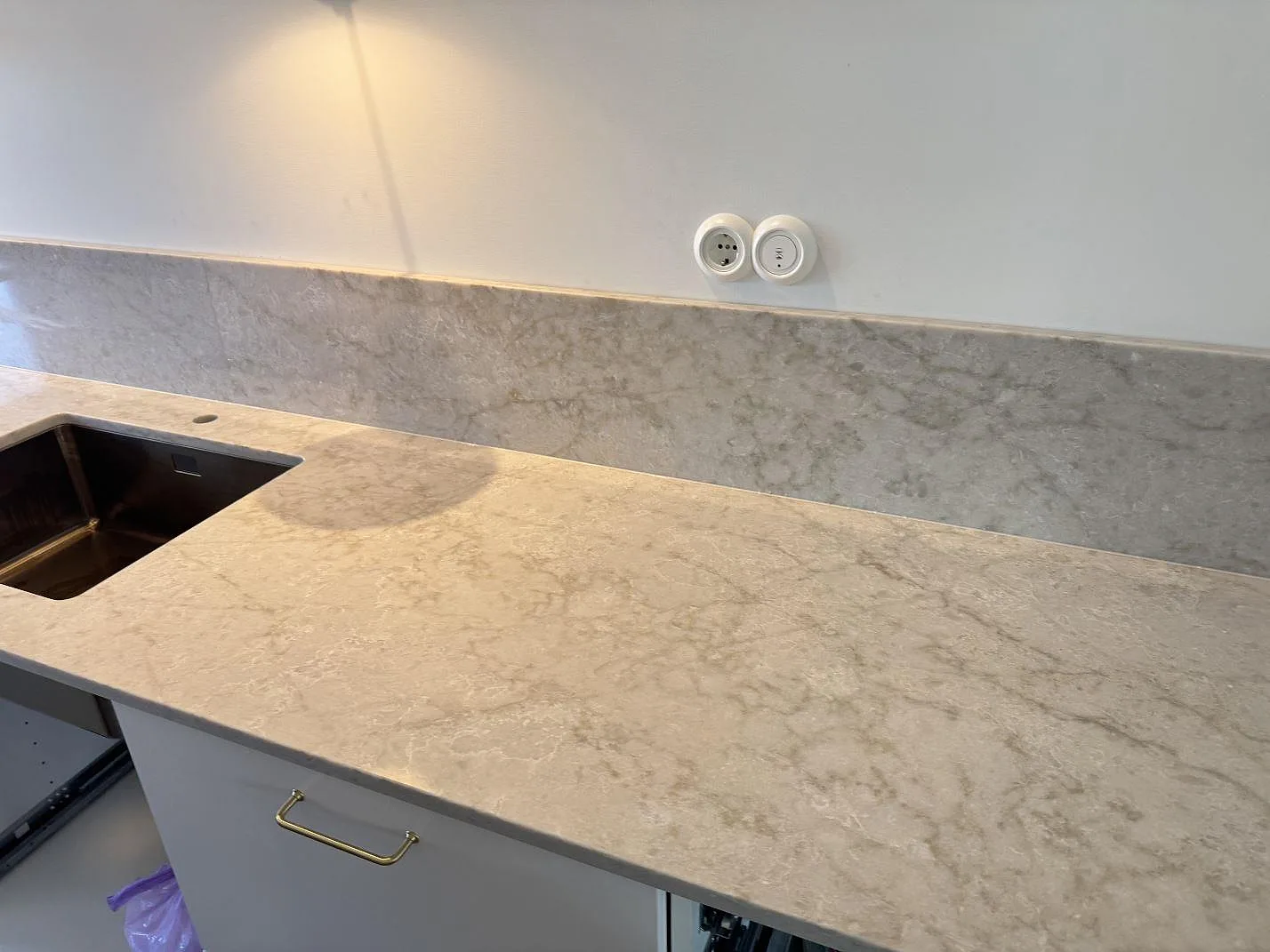 Köksbänkskiva i polerad Technistone Glencoe kvartskomposit med låg stänkkant och rostfri diskho under montering i Malmö.