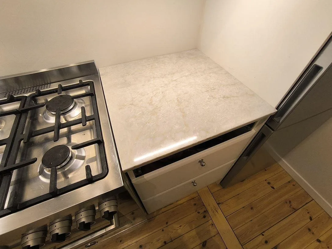 Detalj av polerad Technistone Glencoe bänkskiva vid fristående gasspis och kyl i ett kompakt kök i Stockholm.