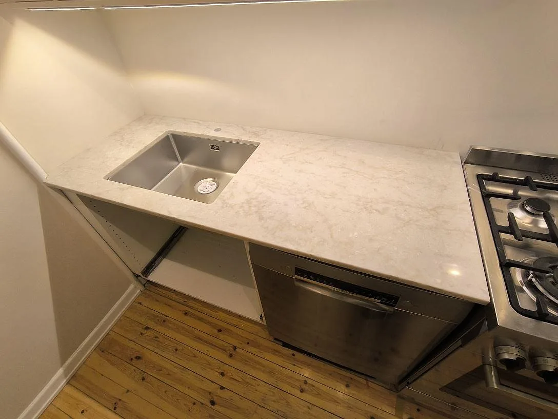 Polerad köksbänkskiva i Technistone Glencoe komposit med ljus ådring och synlig diskho i ett kök under montering i Stockholm.