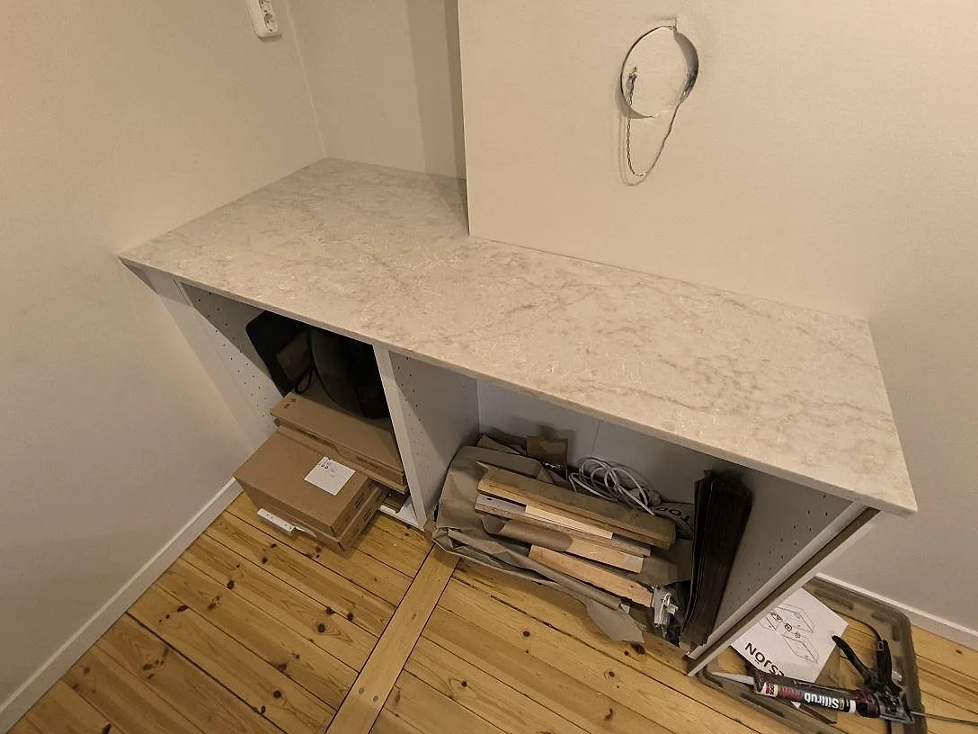 Sidobänk i polerad Technistone Glencoe komposit över öppna köksstommar under montering i Stockholm.
