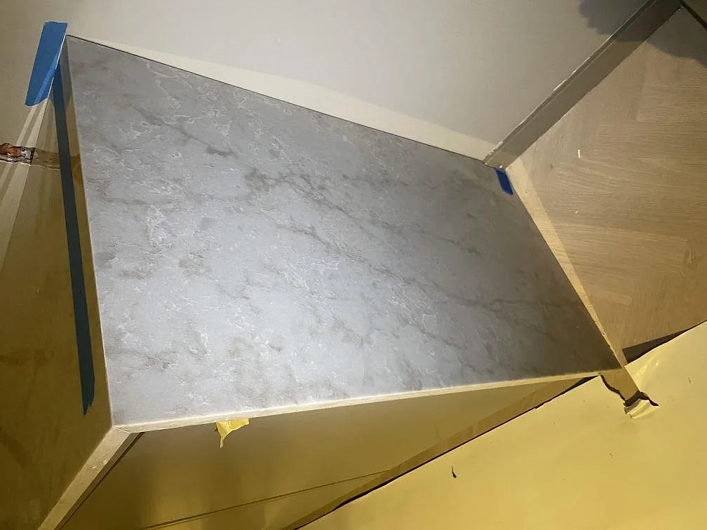Närbild ovanifrån av polerad Technistone Glencoe bänkskiva i ljusgrå komposit med mönstrad ådring på skåpsrad i Stockholm.