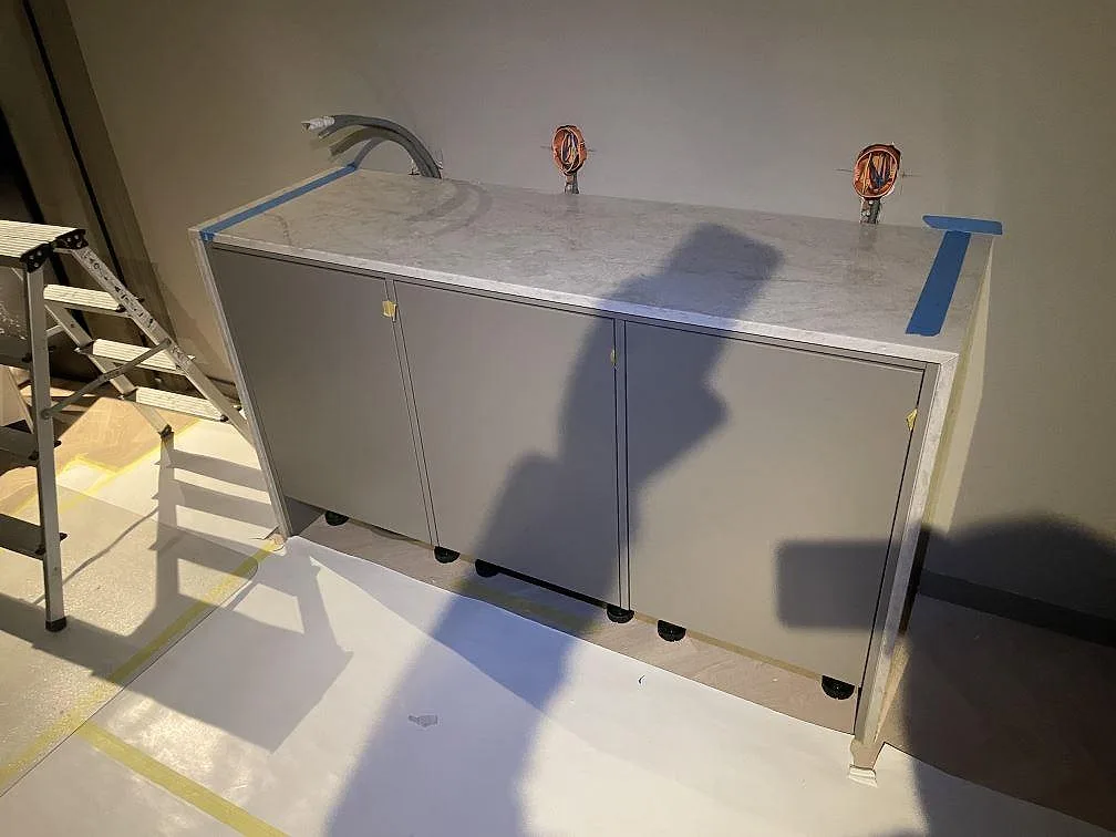 Bänkskiva i polerad Technistone Glencoe, ljusgrå kvartskomposit, monterad på en lång grå skåpsrad i ett badrum under montering i Stockholm.