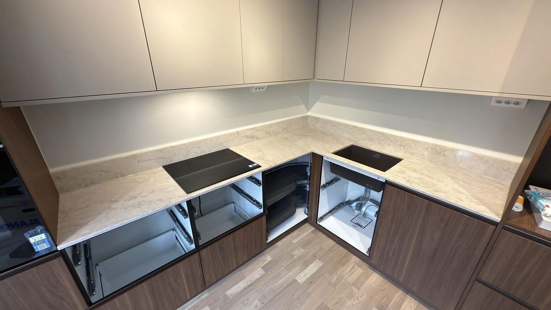 Köksbänkskiva i ljus Technistone Glencoe, kvartskomposit med grå ådring, polerad yta, med underlimmad mörk diskho och induktionshäll i ett L-format kök i Stockholm.
