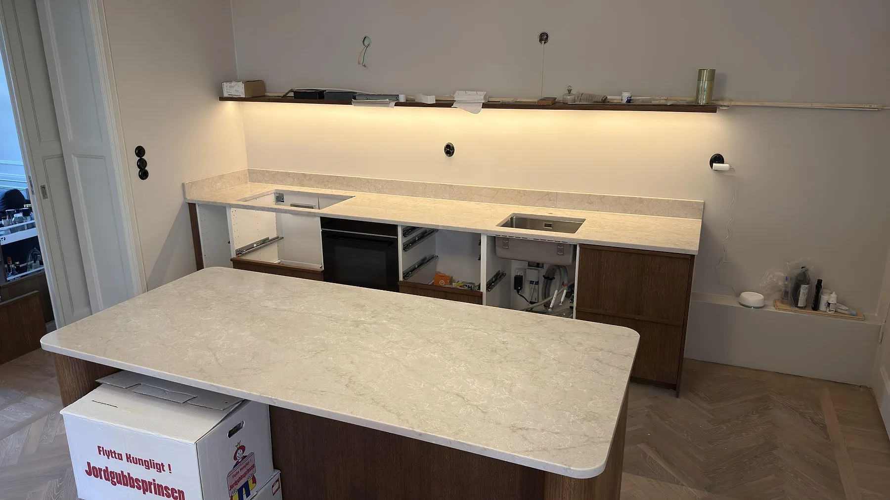 Köksbänkskiva i ljus Technistone Glencoe, polerad kvartskomposit, monterad som stor köksö och bänk längs väggen i ett kök i Stockholm.