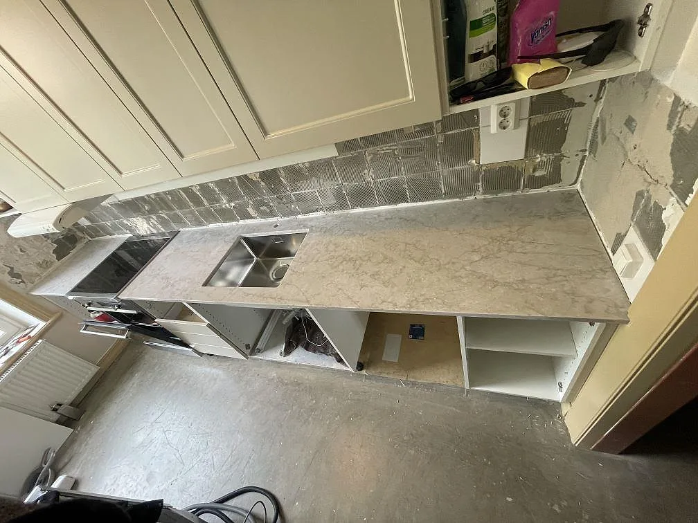 Köksbänkskiva i gråvit Technistone Glencoe komposit, polerad, med diskho och häll i ett kök under montering i Stockholm.