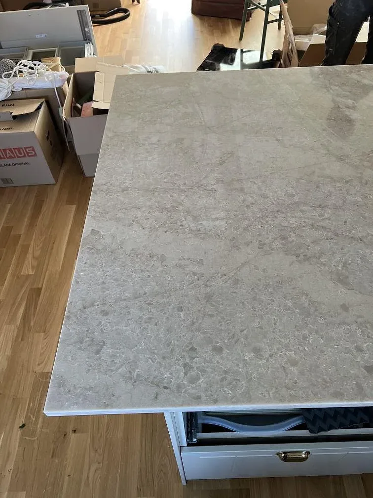 Ytbild av 20 mm polerad Technistone Glencoe på vit köksinredning under montering i Vellinge.