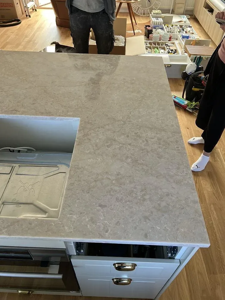 Installerad köksbänkskiva i Technistone Glencoe med urtag för häll och vita lådfronter i Vellinge.