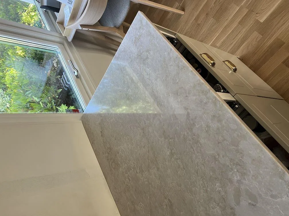 Detalj av polerad Technistone Glencoe som köksbänkskiva framför stora fönster i Vellinge.