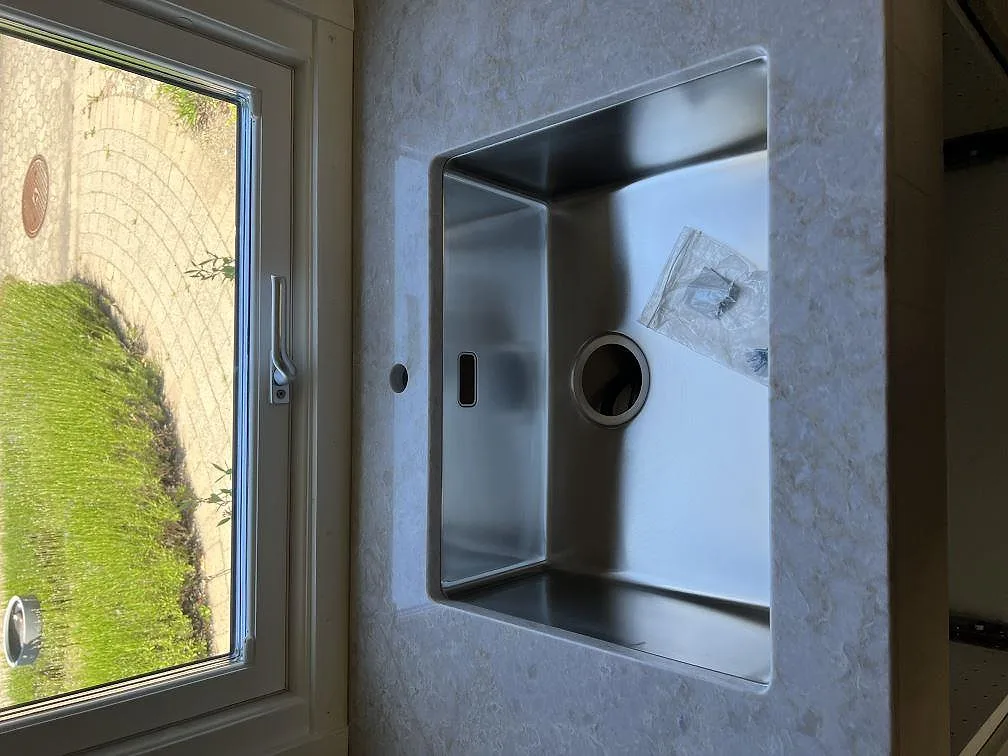 Underlimmad rostfri diskho i polerad Technistone Glencoe vid ett trädgårdsfönster i kök i Vellinge.