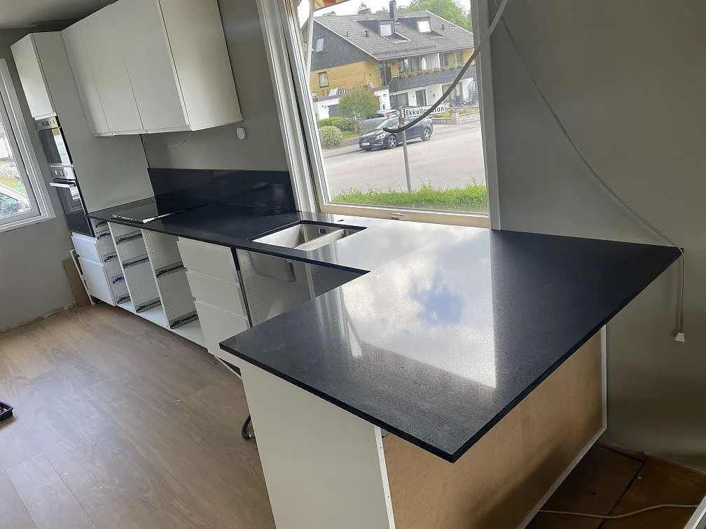 Köksbänkskiva i Technistone Gobi Black, polerad kvartskomposit, med halvö och underlimmad rostfri dubbelho i ett kök i Borås.
