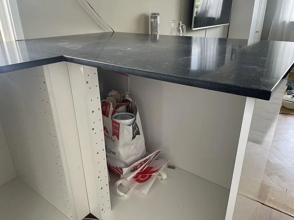Kökshalvö med polerad Technistone Gobi Black bänkskiva på vita köksstommar under montering i Borås.
