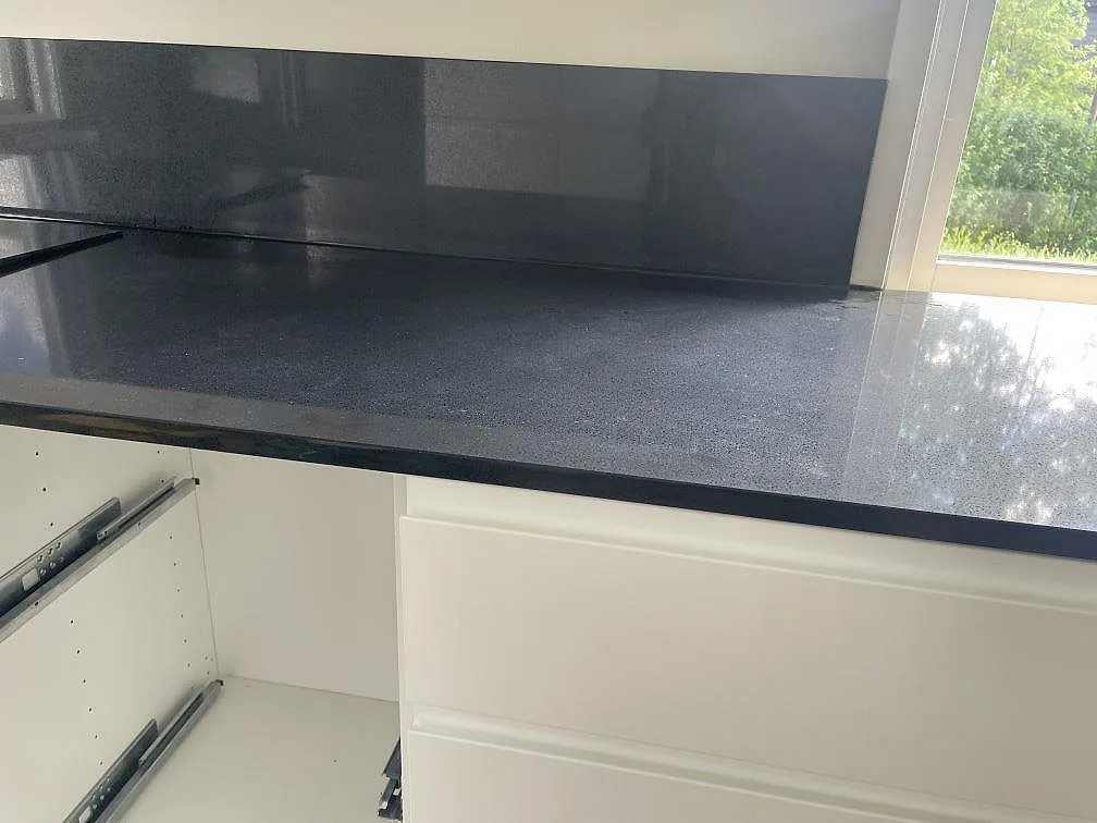 Polerad mörk kompositbänkskiva i Technistone Gobi Black med stänkskydd vid fönster i ett kök i Borås.
