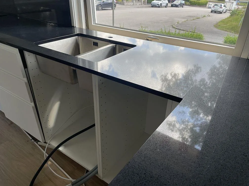 Polerad köksbänkskiva i Technistone Gobi Black med underlimmad dubbelho i rostfritt stål och stora fönster i Borås.