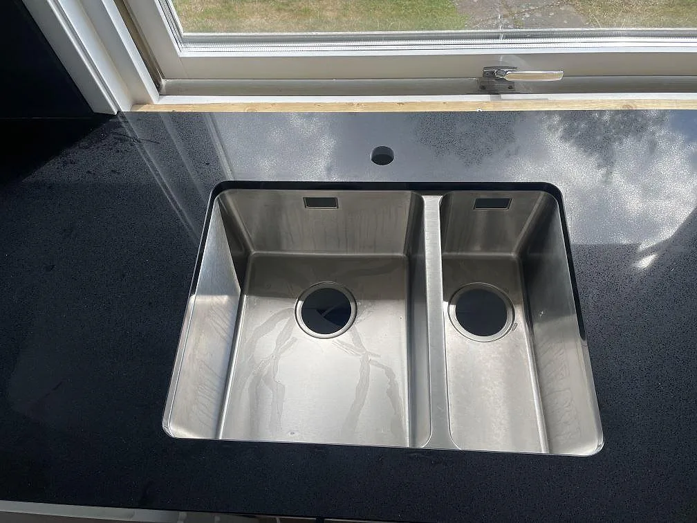 Närbild på underlimmad dubbelho i rostfritt stål i en polerad Technistone Gobi Black bänkskiva i Borås.
