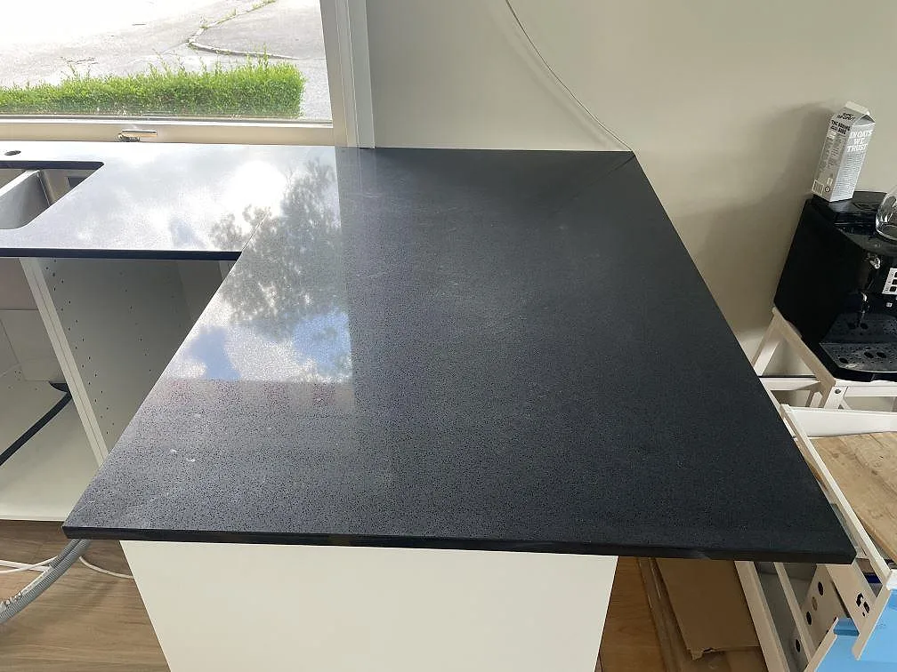 Polerad Technistone Gobi Black bänkskiva i mörk komposit på en kökshalvö med diskho och fönsterljus i Borås.