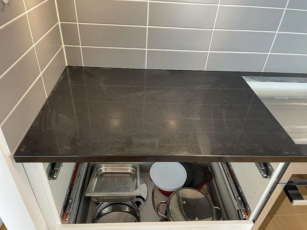 Detalj av polerad Technistone Gobi Black komposit med mörk kornighet, diskhoutsnitt och öppna lådor i Dalby.