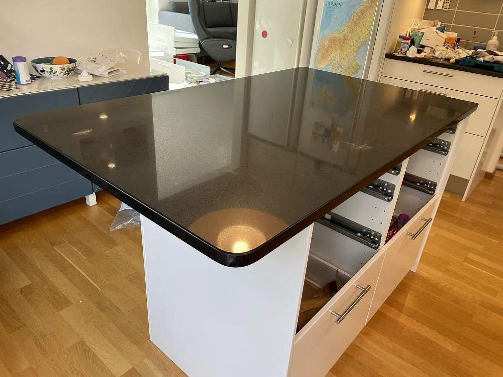 Närbild på köksö i polerad Technistone Gobi Black komposit med rundade hörn och vit stomme i Dalby.